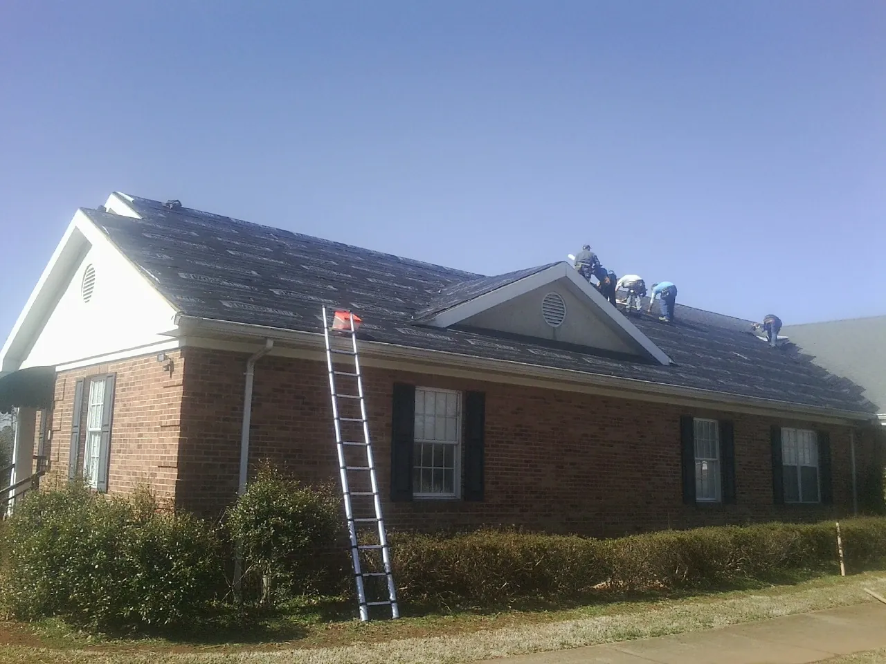 Crew tearing shingles off a brick ranch roof with a ladder set — Emergency Roof Repair work by our crew in Kite