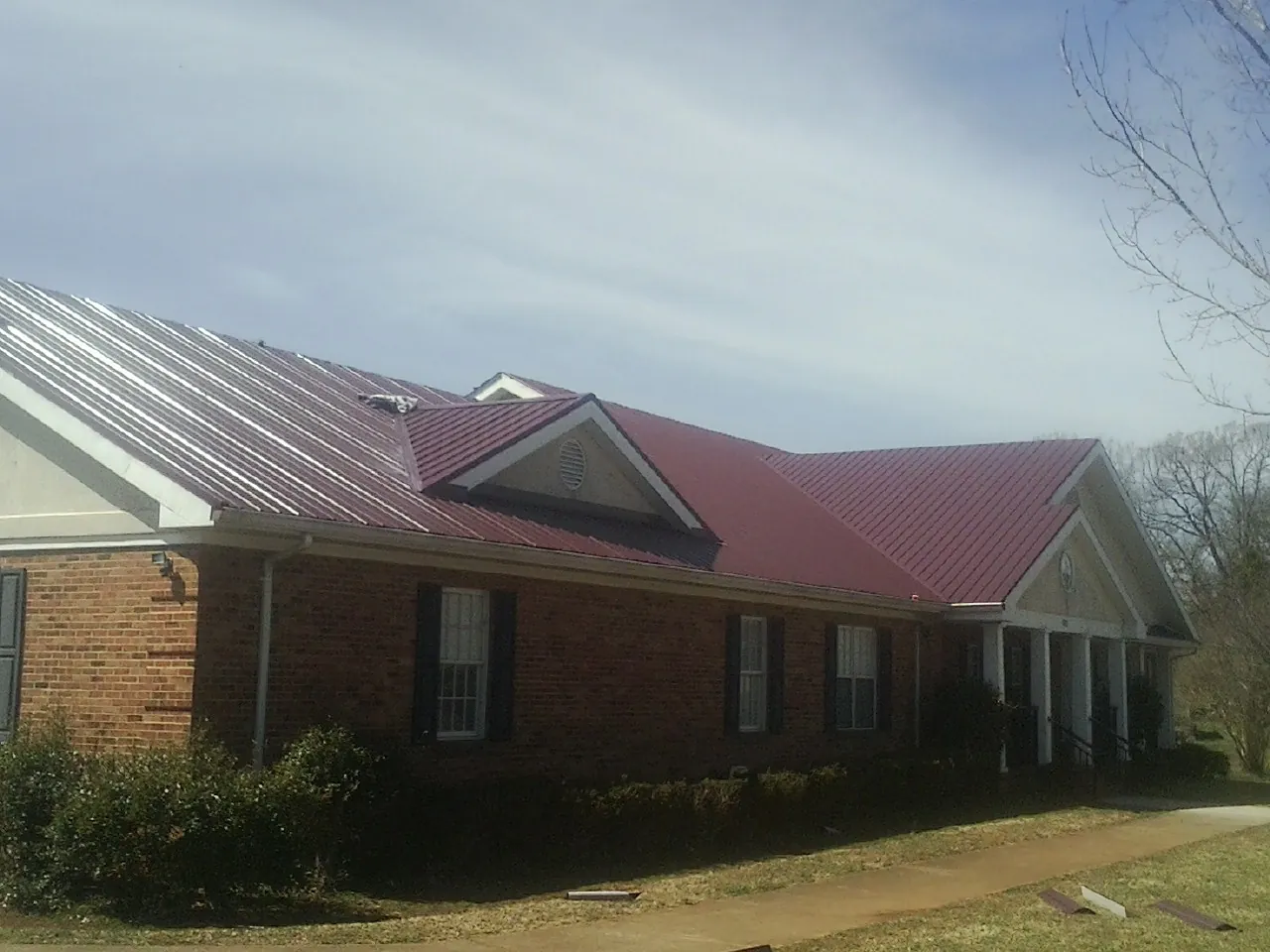 Red metal roof with gabled entries on a long brick building, from a Hail Damage Roof Repair job in Kite