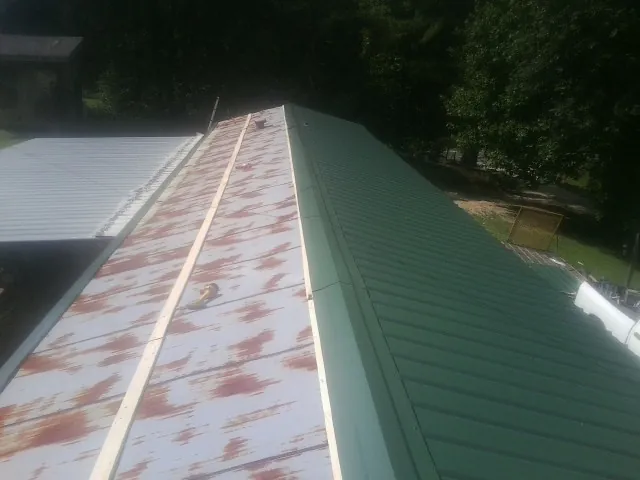 Old rusted panels beside newly installed green metal roofing — Wind Damage Roof Repair by Roofing Brothers in Kite