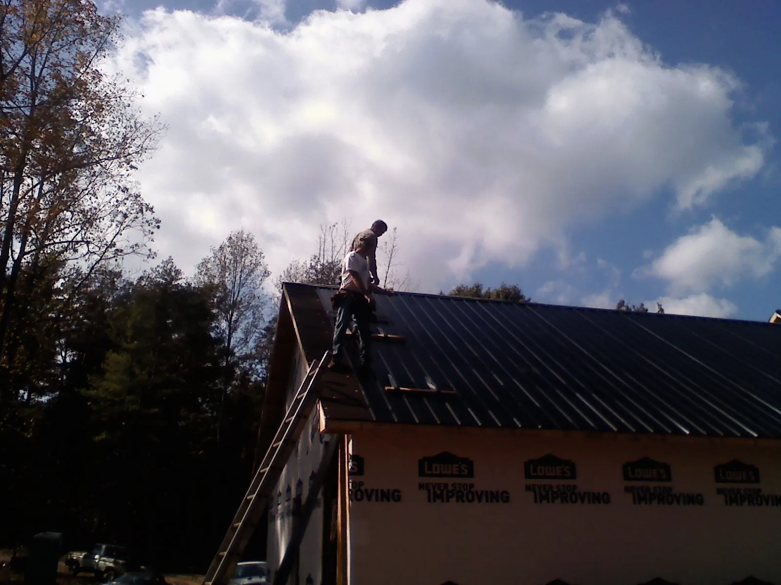 Roofer fastening dark metal panels high against a cloudy sky, from a Roof Inspection job in Kite